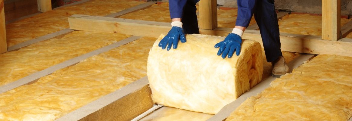 Eine Person dämmt eine Geschossdecke mit Dämmwolle.